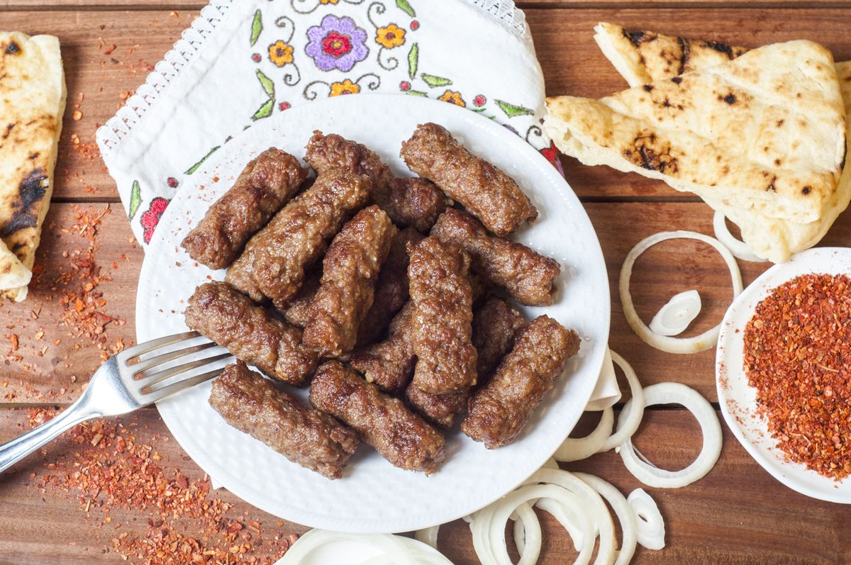 Cevapcici auf einem Teller umgeben von Zwiebeln und Brot